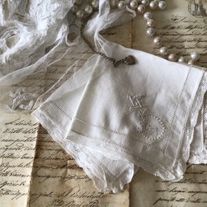 May include: White linen handkerchiefs with embroidered details and lace edging. A silver chain with a heart charm and a string of pearls are placed nearby. The background includes antique documents and lace.