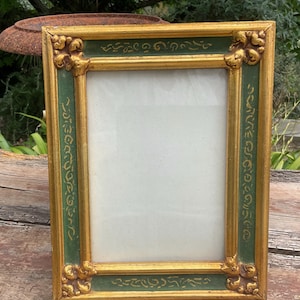 Puede incluir: Marco de fotos ornamentado con acabado dorado y verde. El marco rectangular tiene detalles decorativos en las esquinas y detalles dorados. Las secciones verdes presentan volutas doradas. El marco está vacío, listo para una foto o una obra de arte.