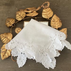 以下が含まれることがあります： 白い刺繍入りハンカチ、スカラップエッジ付き、金色の装飾フレームに葉と花のアクセント付き。 ハンカチは繊細なカットワークが特徴です。