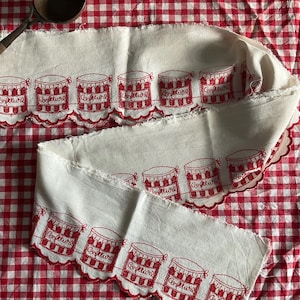 Könnte beinhalten: Weißer Stoff mit rotem Vichy-Muster im Hintergrund. Der Stoff ist mit roten Gläsern mit "Confiture" bestickt und hat einen gewellten Rand. Ein Vintage-Holzlöffel befindet sich in der oberen linken Ecke. Der Stoff ist gefaltet und drapiert.