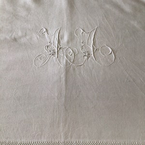 May include: White linen textile with embroidered initials "JJ" in a delicate, cursive script. The embroidery features floral accents. A decorative, stitched border runs along the bottom edge, adding a touch of elegance to the fabric.