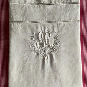 Può includere: Una federa rettangolare in lino bianco con un monogramma ricamato a mano delle lettere SC al centro, circondato da un motivo a ghirlanda floreale. La parte superiore include due file orizzontali di dettagli a giorno con orlo a giorno.