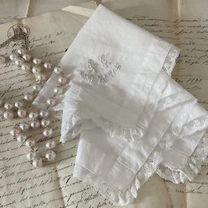 May include: A white cotton handkerchief with delicate lace trim and embroidered floral design. The handkerchief is laid on top of a sheet of old, handwritten paper.