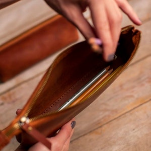May include: A brown leather pencil case with a zipper closure. The case is open and contains several pencils.