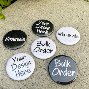 May include: Six round buttons with black and white backgrounds. The buttons have the text "Your Design Here", "Wholesale", "Bulk Order" printed in white on black and black on white.