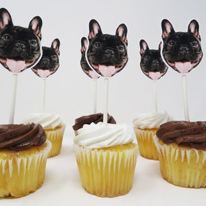 May include: Six cupcakes with white and chocolate frosting, decorated with French bulldog toppers. The cupcakes are on a white surface.