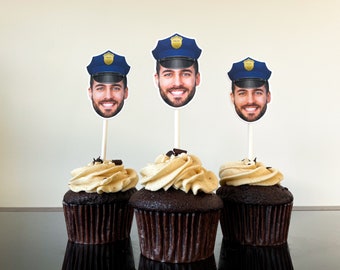 May include: Three chocolate cupcakes with brown frosting and chocolate sprinkles topped with police officer face cutouts. The cutouts have a blue police hat with a gold badge.