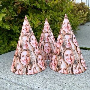 May include: Three conical party hats made of paper, each featuring a repeating pattern of a smiling woman with blonde hair. The hats are arranged in a cluster, displaying multiple instances of the same face printed across the entire surface.