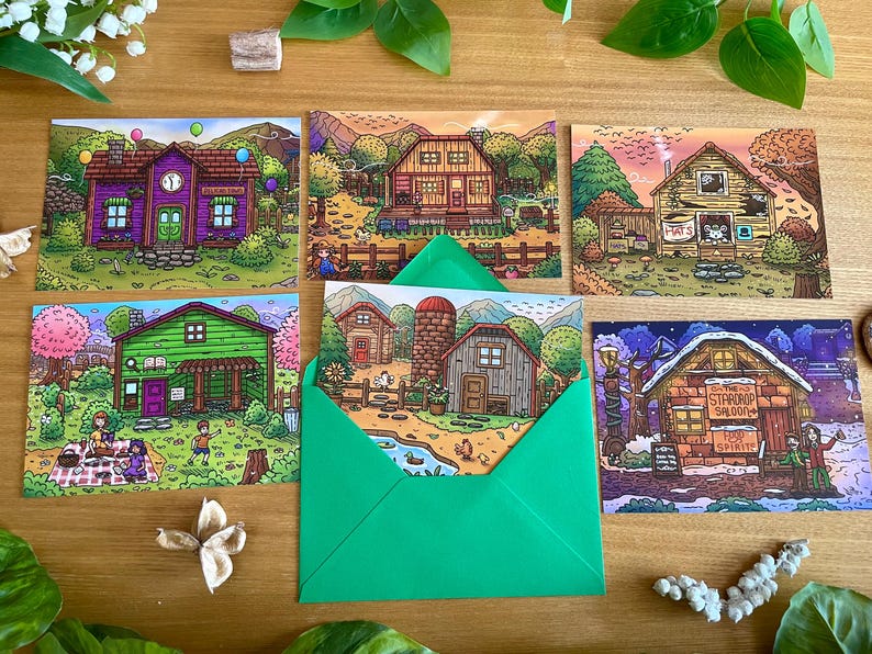 May include: A collection of illustrated postcards featuring colorful drawings of buildings and landscapes. One card is inside a green envelope. The postcards depict scenes with houses, farms, and outdoor settings, with a whimsical, cartoon-like style.