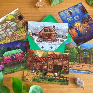 May include: A collection of illustrated postcards featuring colorful scenes of houses, cabins, and a greenhouse. The cards depict various settings, including a snowy landscape, a cozy interior, and a whimsical caravan. The cards are arranged on a wooden surface.
