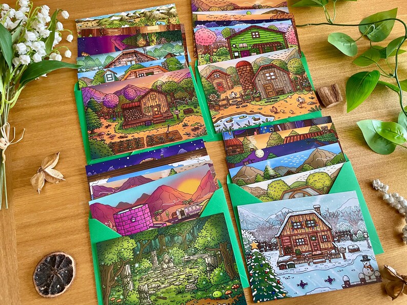 May include: A collection of illustrated greeting cards featuring various landscape scenes, including houses, mountains, and forests. The cards are in green envelopes, arranged on a wooden surface, with floral and botanical accents.
