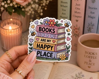 Puede incluir: Una pegatina troquelada que muestra una pila de cuatro libros coloridos con el texto "BOOKS ARE MY HAPPY PLACE" en letras negras. El diseño incluye ilustraciones de pequeñas flores, corazones y dos abejas alrededor de los libros.
