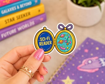 Puede incluir: Una pegatina troquelada con forma de relicario dorado con un lazo morado en la parte superior. El lado izquierdo presenta el texto SCI-FI READER en amarillo sobre un fondo azul. El lado derecho muestra ilustraciones coloridas de planetas, un cohete y un OVNI.