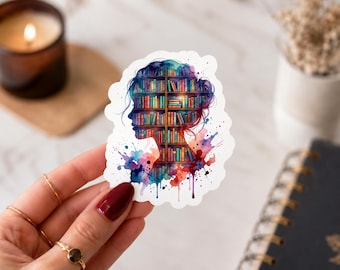 Puede incluir: Una pegatina troquelada que presenta la silueta de una cabeza humana rellena con una colorida ilustración de una estantería de varios niveles llena de libros. El diseño incorpora salpicaduras de acuarela vibrantes en tonos azul, morado, rojo y naranja.