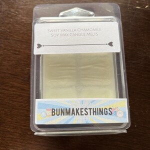 May include: A clear plastic container with a white soy wax candle melt inside. The label reads "Sweet Vanilla Chamomile Soy Wax Candle Melts" and "Bunmakesthings".