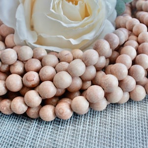 May include: A strand of natural wood beads in a light brown color. The beads are round and smooth, and they are arranged in a pile.