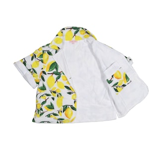 May include: A white short-sleeved jacket with a lemon print. The jacket has a collar and a pocket on the left side.