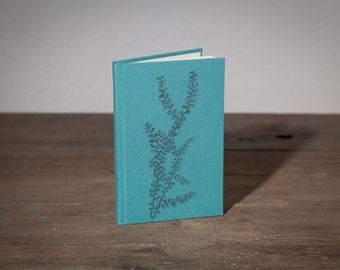 May include: A teal blue linen-covered journal with a floral design embossed on the front cover.