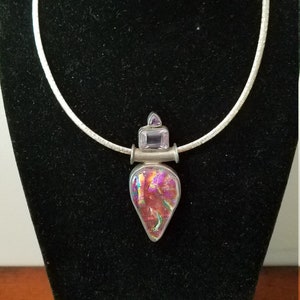 May include: A silver necklace with a pendant featuring a teardrop-shaped iridescent stone surrounded by two smaller amethyst stones.