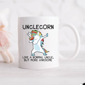 Op de afbeelding: Een witte keramische mok met een zwart-witte illustratie van een eenhoorn die de dab doet. De tekst "Unclecorn" is in zwart boven de eenhoorn gedrukt en de tekst "Like a normal uncle, but more awesome" is in zwart onder de eenhoorn gedrukt.