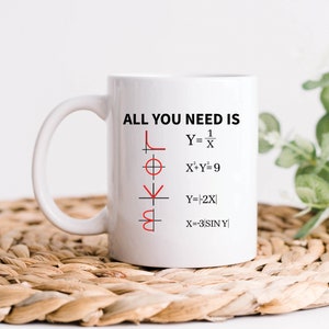 Könnte beinhalten: Eine weiße Keramiktasse mit einer schwarzen Umrandung des Wortes "LOVE", das durch mathematische Gleichungen gebildet wird. Der Text "ALL YOU NEED IS" ist über den Gleichungen gedruckt.