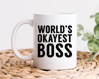 May include: White ceramic coffee mug with black text that reads "World's Okayest Boss".