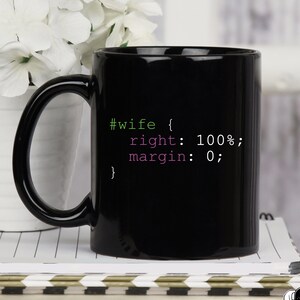 Könnte beinhalten: Schwarze Kaffeetasse mit einem weißen Design, auf dem "#wife { right: 100%; margin: 0; }" steht. Die Tasse steht auf einem Stapel Notizbücher.