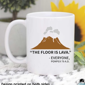 May include: White ceramic coffee mug with a brown volcano illustration and the text "THE FLOOR IS LAVA." - EVERYONE, POMPEII 79 A.D.