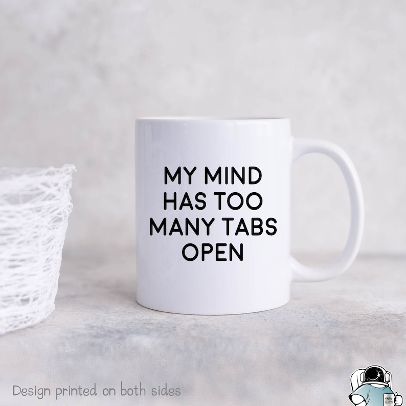 May include: White ceramic coffee mug with black text that reads "My mind has too many tabs open".