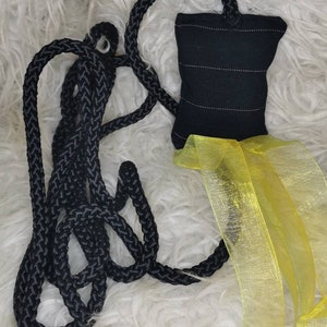 Op de afbeelding: Een zwart gevlochten touw met een zwarte stoffen tas en een geel doorschijnend lint.