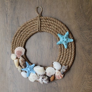 May include: A brown rope wreath decorated with seashells and blue starfish. The wreath is hanging on a wooden background.