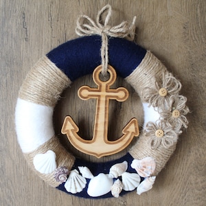 May include: A nautical themed wreath with a wooden anchor, burlap rope, white and blue fabric, and seashells.