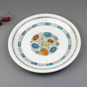 Puede incluir: Plato de cena de cerámica blanca con un diseño floral azul, amarillo y naranja. El plato tiene un borde blanco y negro.