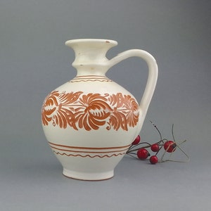 A small vintage ceramic jug covered with white enamel with a hand-carved floral design.