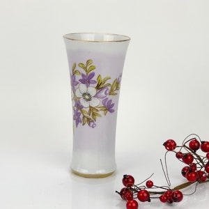 May include: A white porcelain vase with a purple and gold floral design. The vase has a flared top and a narrow base.