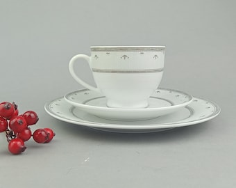 May include: A white teacup and saucer set with a silver trim and floral design. The saucer has a silver rim and a floral pattern.