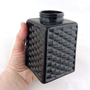 May include: A black glass jar with a diamond pattern on the sides. The jar has a wide mouth and a smooth, rounded top.
