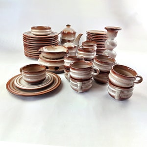 May include: A set of brown and white striped ceramic teacups and saucers, a teapot, and a sugar bowl. The set is arranged on a white surface.