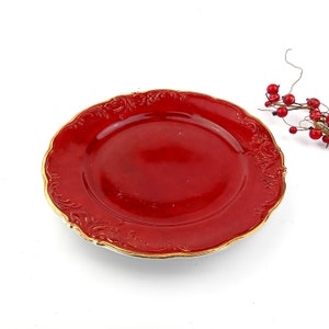 Può includere: Un piatto in ceramica rosso con un bordo dorato e un intricato disegno floreale. Il piatto ha un bordo ondulato.