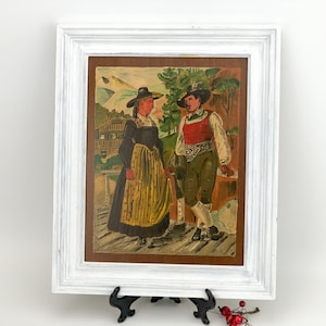 Pode incluir: Uma pintura emoldurada que retrata um homem e uma mulher com roupas tradicionais em pé em frente a uma cena de montanha. A pintura é feita em um estilo colorido com um fundo marrom.