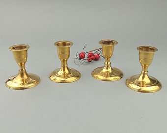 May include: Four gold-toned metal candle holders with a simple design. Each holder has a round base and a cup-shaped top for holding a candle.