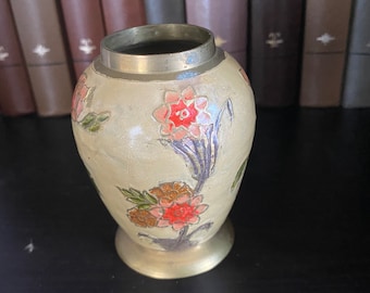 May include: A small, cream-colored ceramic vase with a brass rim. The vase is decorated with hand-painted floral designs in shades of pink, green, and purple.