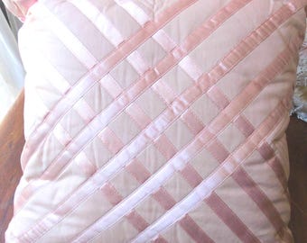 HAND-EMBROIDERED CUSHION with crisscross pattern and stiff satin ribbons on a matte pink, faded marble background