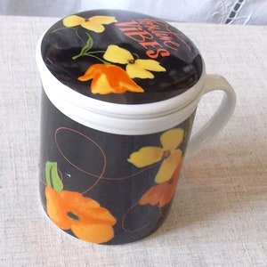 Peut inclure: Mug en céramique noire avec une anse et un couvercle blancs, décoré de motifs floraux orange et jaunes. Le couvercle porte l'inscription "Positive Vibes" en orange. Le mug est conçu pour les boissons chaudes.