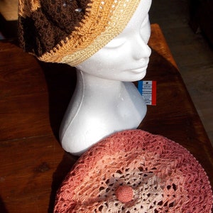 May include: Two crocheted hats, one brown and beige with a white mannequin head, the other pink and peach.