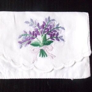 May include: White handkerchief with a scalloped edge and a purple floral embroidery design. The embroidery features a bouquet of purple flowers with green leaves and a pink bow.