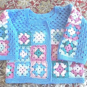 Puede incluir: Una chaqueta de punto de color azul claro con abertura frontal. La chaqueta está hecha con cuadrados de abuela en tonos de rosa, blanco y turquesa.