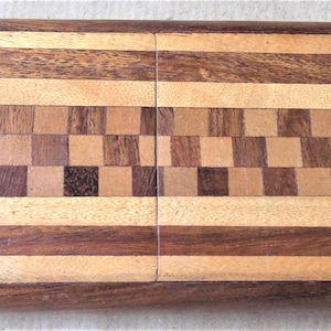 Könnte beinhalten: Eine rechteckige Holzkiste mit Scharnierdeckel. Die Kiste besteht aus verschiedenen Holztönen, darunter Dunkelbraun, Hellbraun und Beige. Der Deckel hat ein Schachbrettmuster und horizontale Streifen.