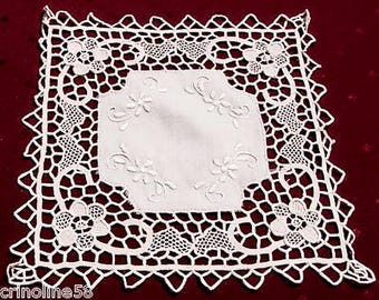 Puede incluir: Doily de encaje blanco tejido a crochet con un delicado diseño floral. El doily tiene forma cuadrada con bordes festoneados y patrones intrincados.
