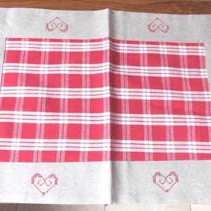 May include: A rectangular red and white checked tablecloth with a grey border. The border has embroidered red hearts at each corner and the text "les collections crinolines pomponnettes" in the upper left corner.